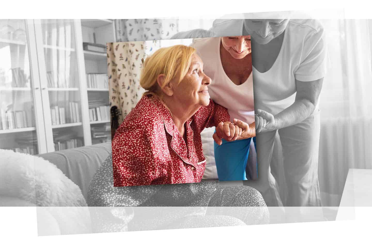 Eine dankbare Seniorin stützt sich auf dem Arm einer Pflegerin ab, um mit ihrer Hilfe vom Sofa aufzustehen.