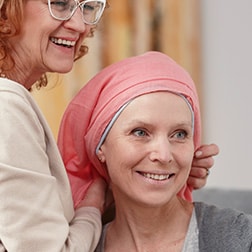 Eine Angehörige bindet ein rosa Kopftuch um den Kopf ihrer lächelnden Tochter.